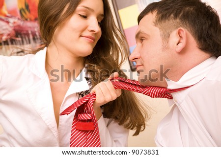 Sexual young woman in formal suit holding in fist tie of her colleague