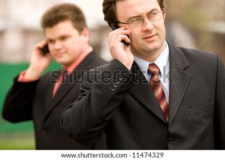 Two businessmen calling by mobile over blurred house on background