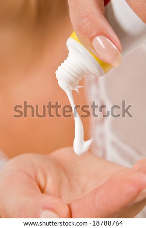Pretty girl pressing plastic tube with cosmetic cream onto palm