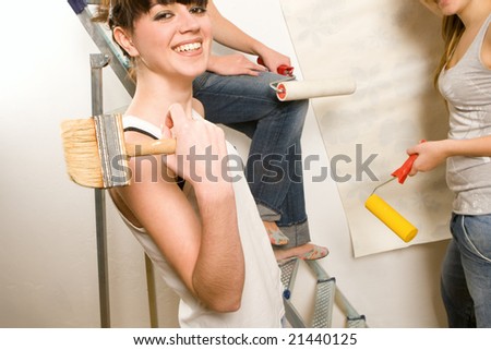 Young pretty girls applying wallpapers on walls