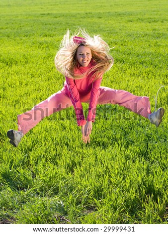 Beautiful young woman jumps above green meadow