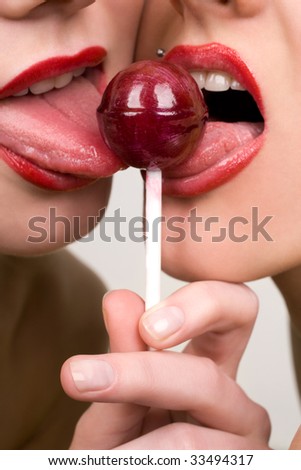 Two sweet female models kissing through lollipop