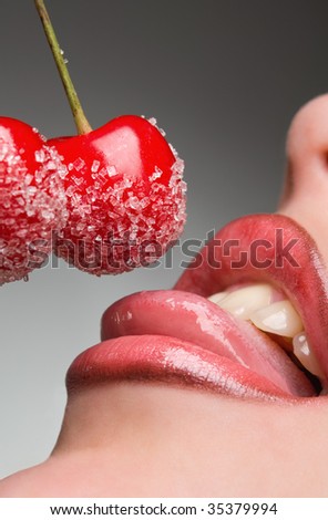 young woman\'s mouth with red cherries covered with sugar