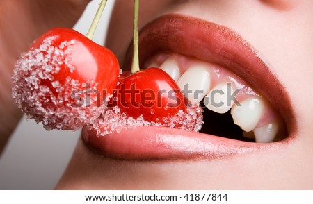 young woman's mouth with red cherries covered with sugar