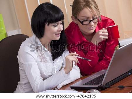 Two pretty young women at workplace discuss the business, are looking at the monitor