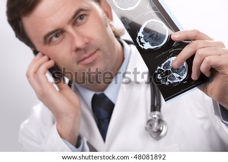 Doctor is checking  x-ray computed tomography, while talking on a cellphone. Horizontal studio shot.