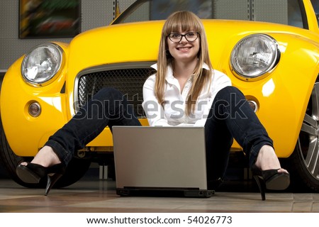 Pretty girl holding laptop sitting against of yellow sport car