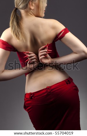 Rear view of pretty young girl in red suit, unfastening the corset, with long red nails