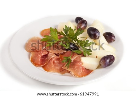 Smoked meat beef slices with melon cubes and grapes on ceramic plate