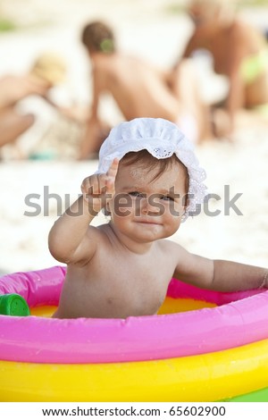 Portrait of cute little baby girl in the inflatable swimming pool showing by finger attention