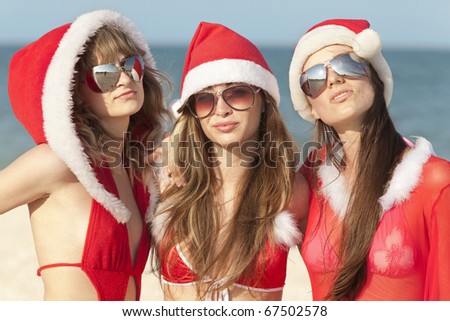 Three happy girls in Santa Clause suit having fun on the beach