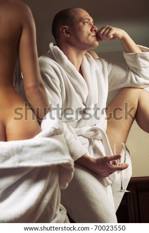 Erotic scene of semi-nude girl and brooding man in with a glass of champagne
