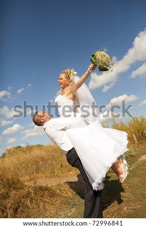 Groom carrying bride in his arms in eared field
