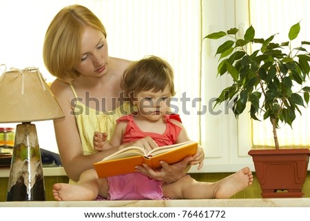 Young mother with her daughter reading book at home