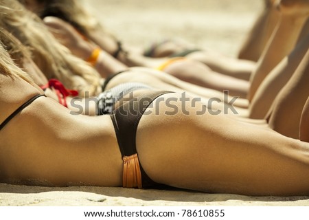 Photo of several girls in bikini lying on sandy beach and tanning in the bright summer sun