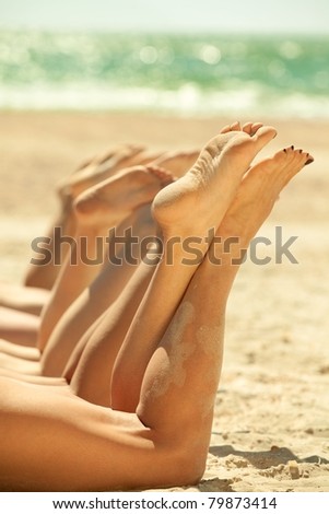 Legs of several girls lying on sandy beach and tanning in the bright summer sun