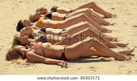 Photo of several girls in bikini lying on sandy beach and tanning in the bright summer sun
