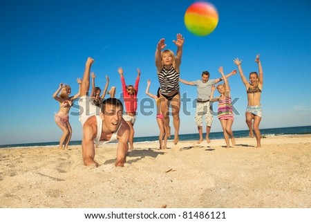 Group of young joyful people playing volleyball on the beach