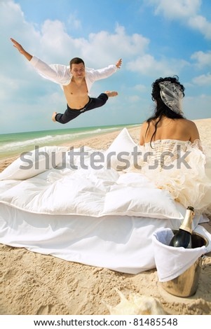 Happy groom flying on bed to his sweetheart on the beach
