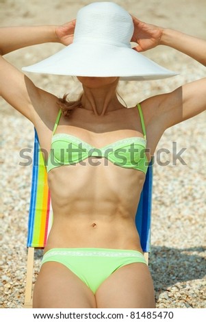 Portrait of young woman sitting in chaise longue  and hiding her face behind her white hat