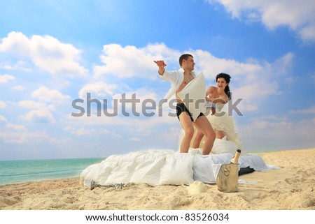 Portrait of happy newlywed couple fighting with pillows in bed on the beach