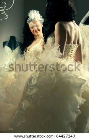 A young woman looking at mirror has in white dress laced up from the back.