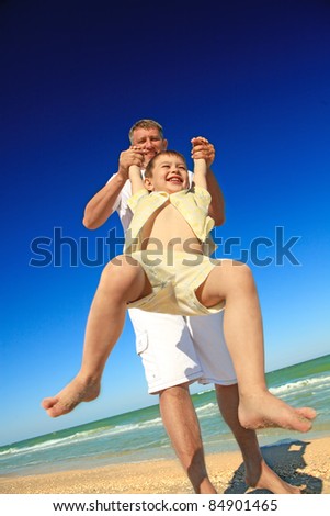 A happy boy tossed into the blue sky by his father at beach