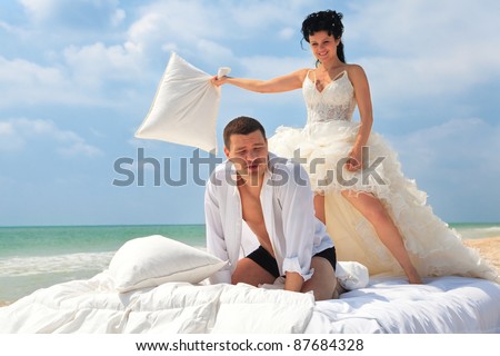 Portrait of happy newlywed couple fighting with pillows in bed on the beach