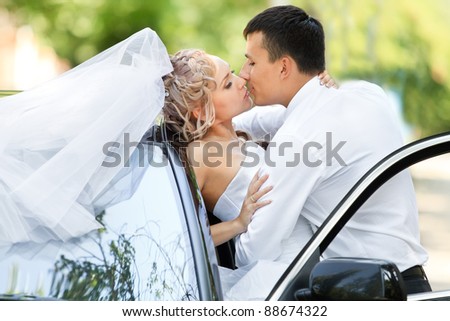 Happy bride and groom kissing next to wedding car