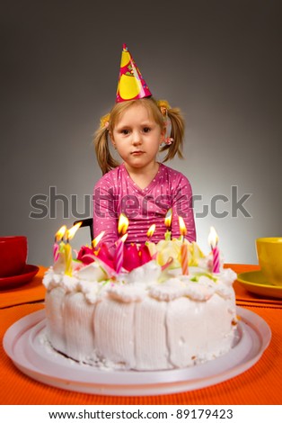 Little sad girl sitting in front of birthday cake