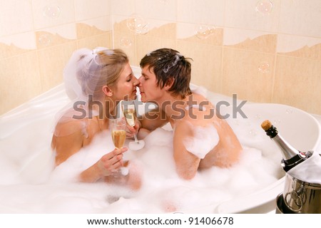 A young beautiful couple is enjoying a bath with champagne in a glass and kissing. Bubbles are floating in the air