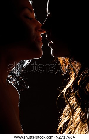 Silhouette of two sexy woman kissing in darkness through light
