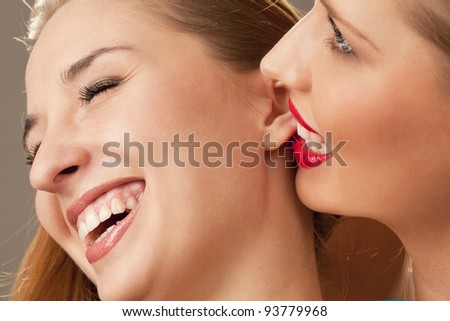 Two young females together, one whispering into the others ear