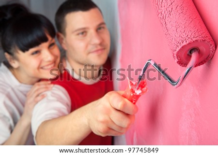 Lovely young couple of workers painting a wall with roller (focus on  roller)