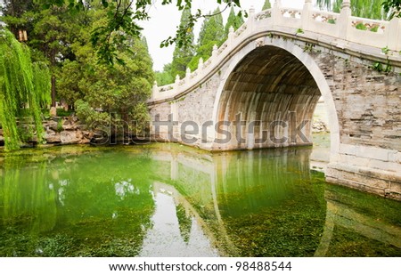 Old style stone Chinese arch bridge in a green garden pond in Beijing, China