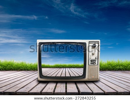 old television on wooden terrace with fresh spring green grass and blue sky