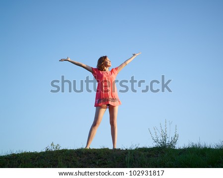 The young woman jumps up on a green hill against the dark blue sky