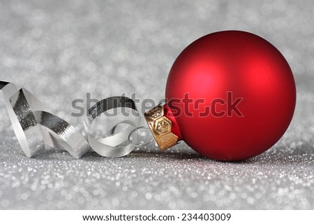 Red Christmas ornament with curled ribbon on a silver background
