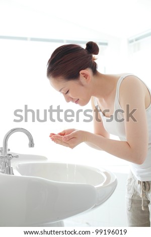 Pretty young woman washing her face at a wash basin