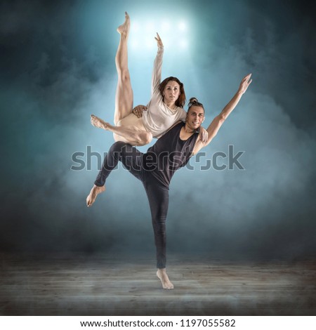 Two people, dancers, woman and man in dynamic action figure pose under light on the grunge background.
