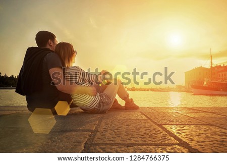 Happy couple of lovers relaxing on the sea pier under sunset sun light at evening time.