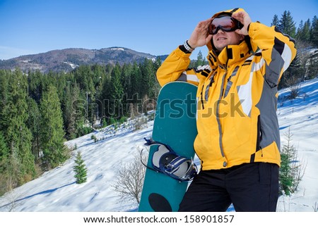 Men in goggles stay with snowboard on the top of mountain