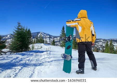 Men in goggles stay with snowboard on the top of mountain