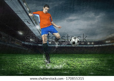 Football player with ball in action under rain in stadium