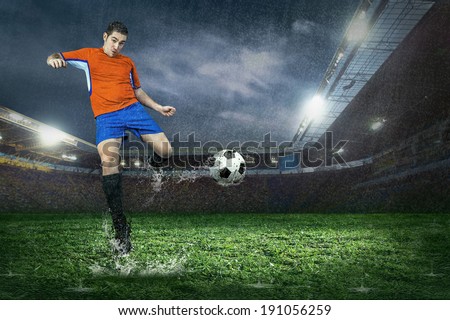 Football player with ball in action under rain in stadium
