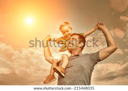 Son seating on the father under beautiful sky with sun