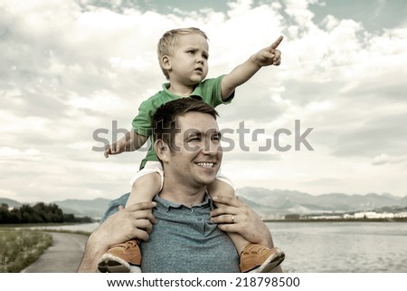 Son seating on the father under beautiful sky