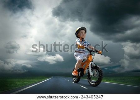 Child seating on the orange bicycle and travelling on the non-urban road under sky