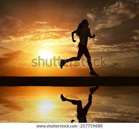 Beautiful silhouette of female running on road under sky with sun light and reflection in water