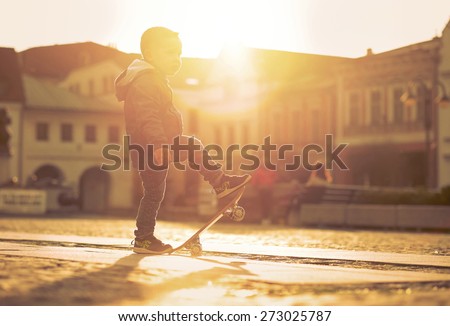 Child with skateboard on the street at sunset light.